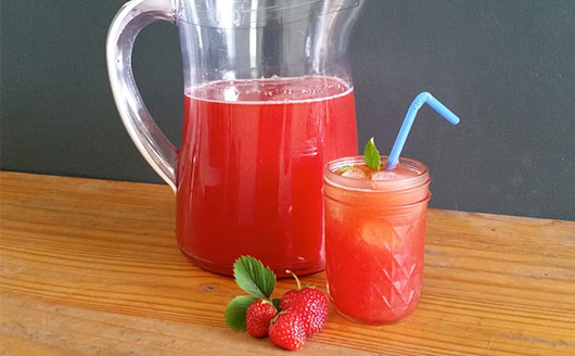 A pitcher of strawberry water next to fresh strawberries