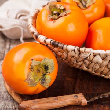 Large persimmon on table next to bowl of persimmons