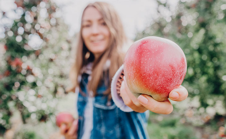 Photo of woman offering an apple picked from a tree